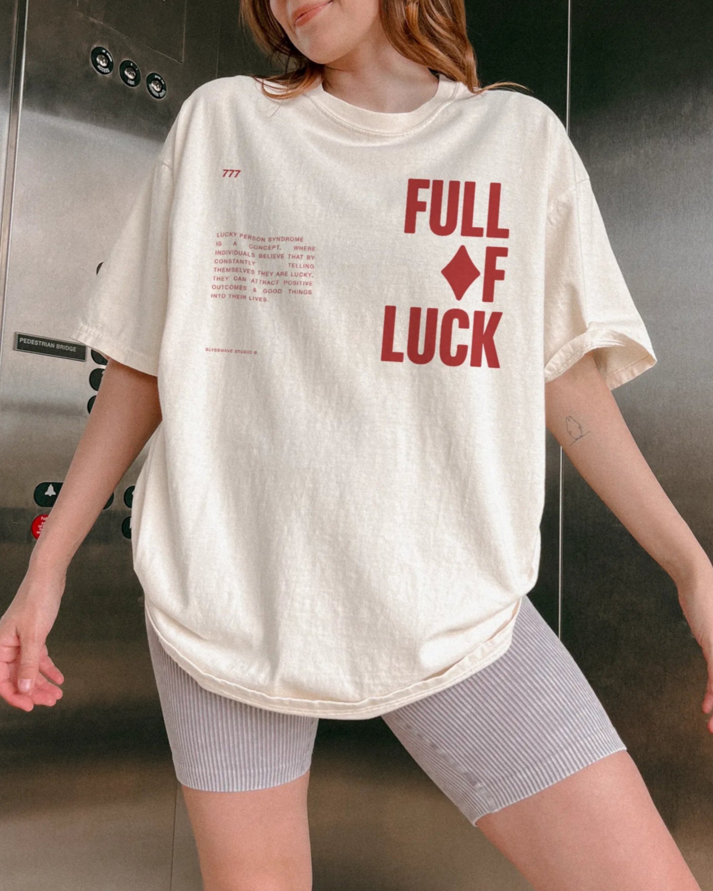 Person wearing a white t-shirt with 'FULL OF LUCK' text in red inside an elevator.